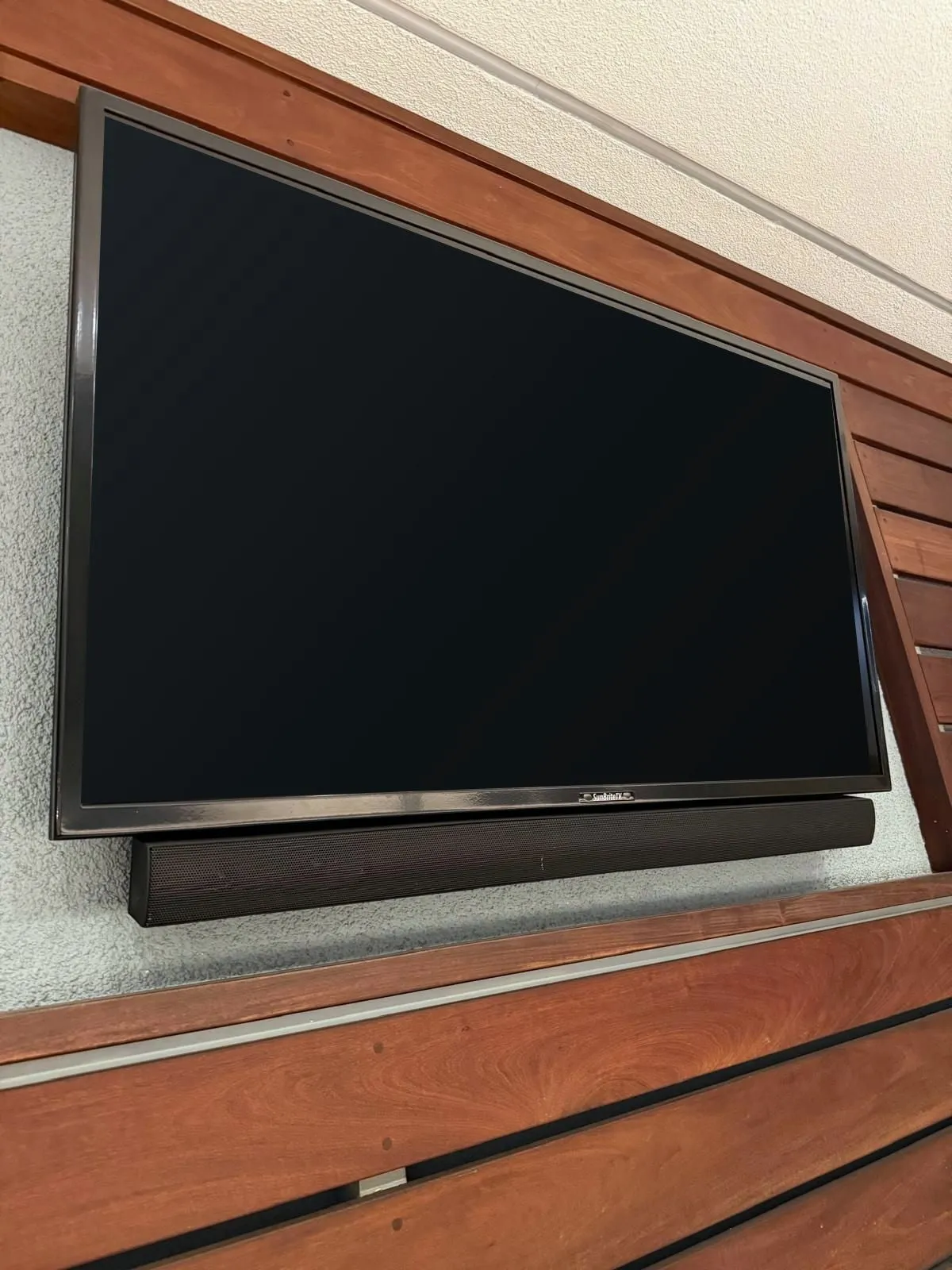Soundbar mounted level directly beneath a wall-mounted TV on a slatted wood wall