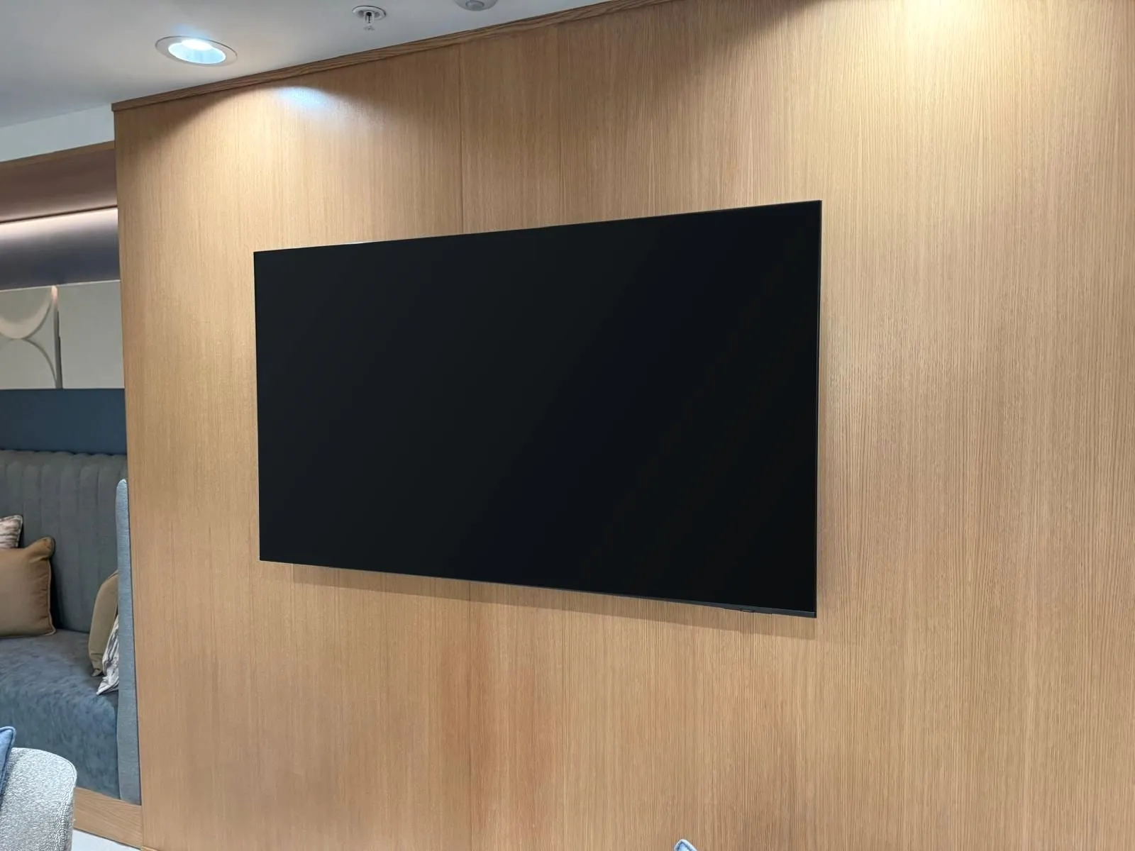 Wall-mounted TV sitting flush on a light oak panel wall in a lounge